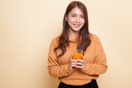 Young Asian woman drink orange juice on beige backgroundの写真素材