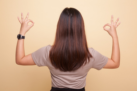 Back view of Asian woman show double OK hand sign on beige backgroundの写真素材
