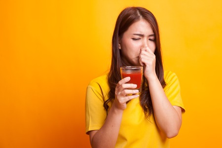 Young Asian woman hate tomato juice in yellow dress on yellow backgroundの写真素材