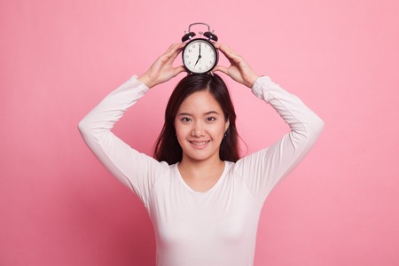 Young Asian woman smile with a clock on pink backgroundの写真素材