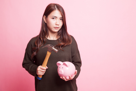 Asian woman with pig coin bank and hammer on pink backgroundの写真素材