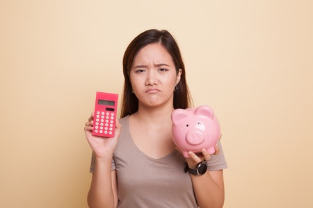 Unhappy Asian woman with calculator and piggy bank on beige backgroundの写真素材