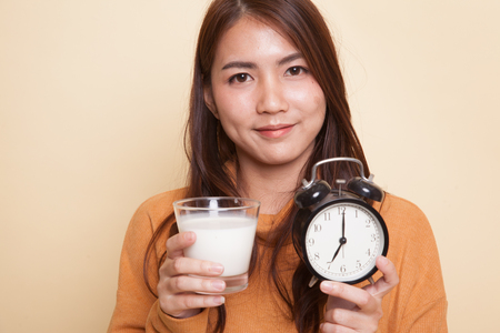 Healthy Asian woman drinking  glass of milk hold clock on beige backgroundの写真素材