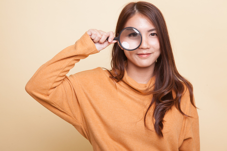 Young Asian woman with a magnifying glass on beige backgroundの写真素材