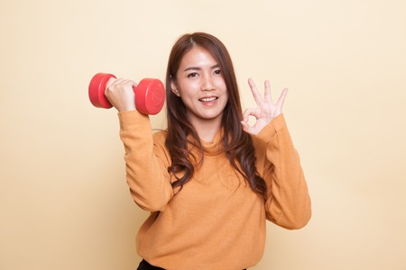 Healthy Asian woman show OK with dumbbells on beige backgroundの写真素材