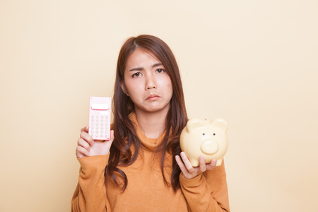 Unhappy Asian woman with calculator and piggy bank on beige backgroundの写真素材