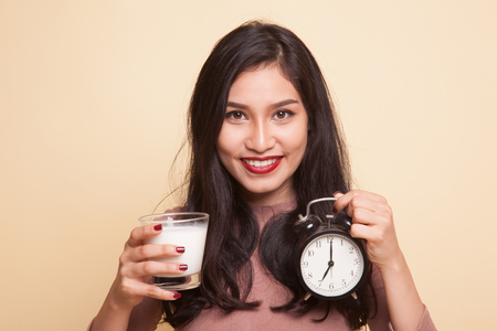 Healthy Asian woman drinking  glass of milk hold clock on beige backgroundの写真素材