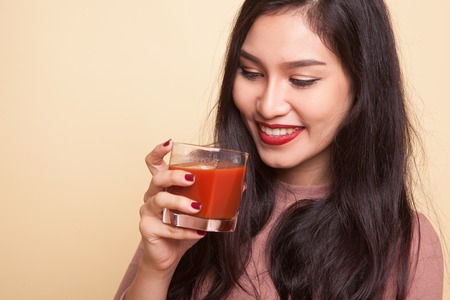 Asian woman with a clock drink orange juice on beige background