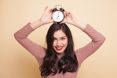 Young Asian woman smile with a clock on beige backgroundの写真素材