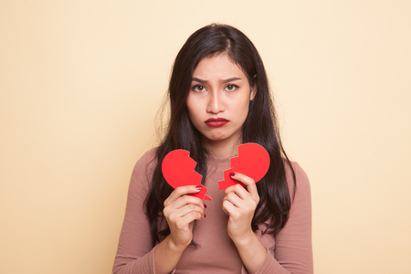 Beautiful young Asian woman with broken heart on beige backgroundの写真素材