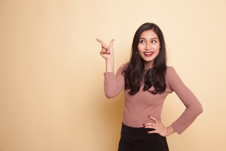 Young Asian woman smile and point on beige backgroundの写真素材