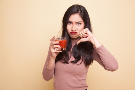 Young Asian woman thumbs up with tomato juice on beige backgroundの写真素材