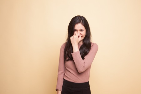 Young Asian woman  holding her nose because of a bad smell on beige background