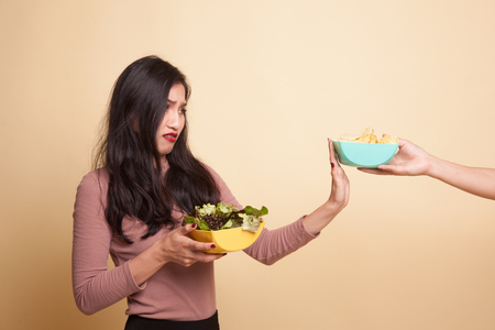 Young Asian woman with potato chips and salad on beige backgroundの写真素材