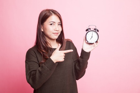Young Asian woman point to a clock on pink backgroundの写真素材