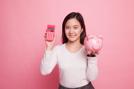 Asian woman with calculator and piggy bank on pink backgroundの写真素材