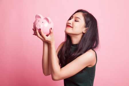 Young Asian woman kiss  a pink coin bank on pink backgroundの写真素材