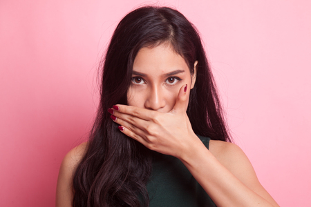 Young Asian woman close her mouth with hand on pink backgroundの写真素材