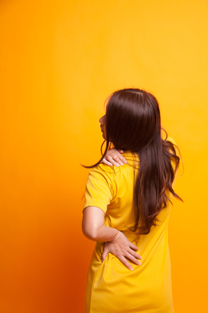 Young Asian woman got back pain in yellow dress on yellow backgroundの写真素材