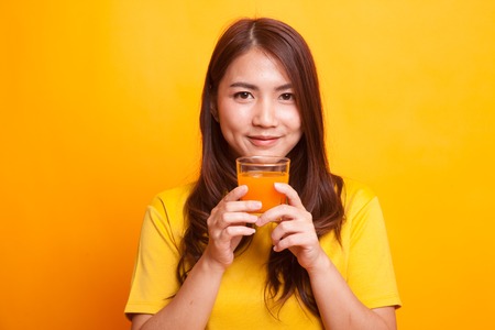 Young Asian woman drink orange juice in yellow dress on yellow backgroundの写真素材