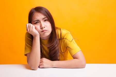 Asian girl is getting bore in yellow dress on yellow background