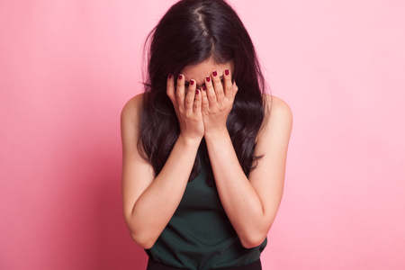 Sad young Asian woman cry with palm to face on pink backgroundの写真素材