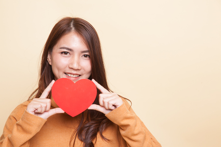 Asian woman with red heart on beige backgroundの写真素材