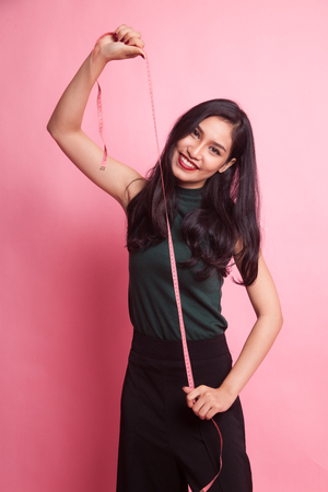 Young Asian woman with measuring tape on pink backgroundの写真素材