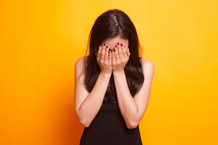 Sad young Asian woman cry with palm to face on yellow backgroundの写真素材