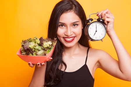 Young Asian woman with potato chips and salad on yellow backgroundの写真素材