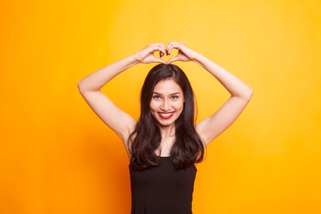 Young Asian woman show with phone gesture on yellow background