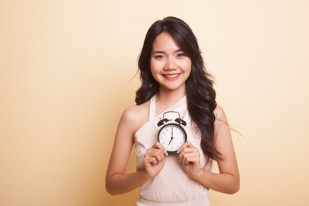 Young Asian woman smile with a clock  on beige backgroundの写真素材