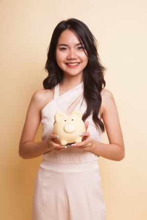 Young Asian woman with a pig coin bank  on beige backgroundの写真素材