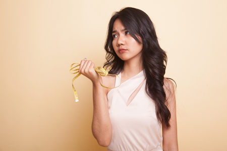 Unhappy young Asian woman with measuring tape  on beige backgroundの写真素材