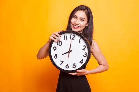 Happy Young Asian woman with a clock on yellow backgroundの写真素材