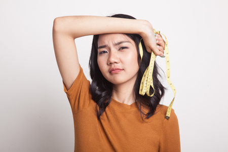 Unhappy young Asian woman with measuring tape on white backgroundの写真素材