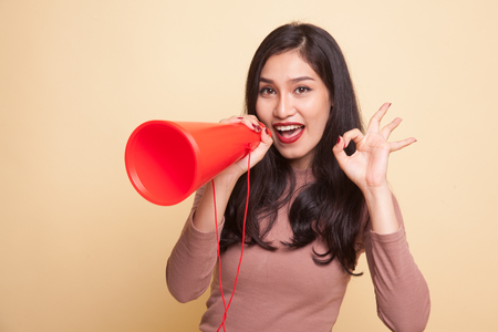 Beautiful young Asian woman show OK  announce with megaphone on beige backgroundの写真素材