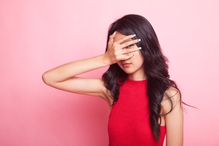 Beautiful young Asian woman peeking through fingers on pink background