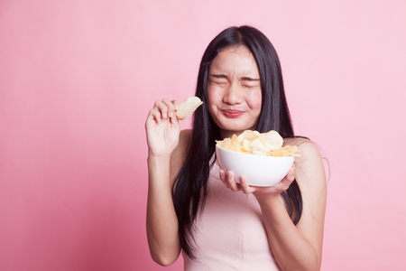 Young Asian woman eat potato chips on pink backgroundの写真素材