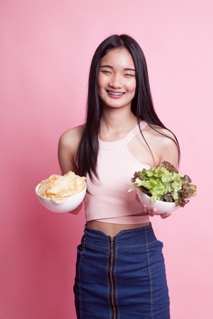 Young Asian woman with potato chips and salad on pink backgroundの写真素材