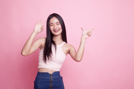 Young Asian woman point and show OK on pink background