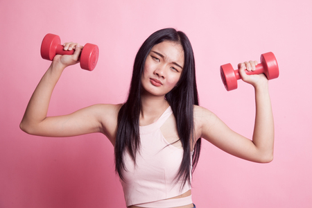 Exhausted Asian woman with dumbbells on pink backgroundの写真素材