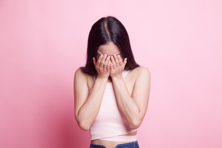 Sad young Asian woman cry with palm to face on pink backgroundの写真素材