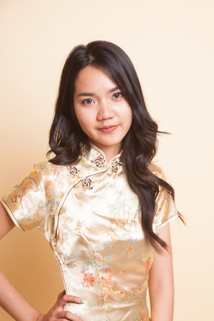Portrait of Asian girl in golden chinese cheongsam dress on beige backgroundの写真素材