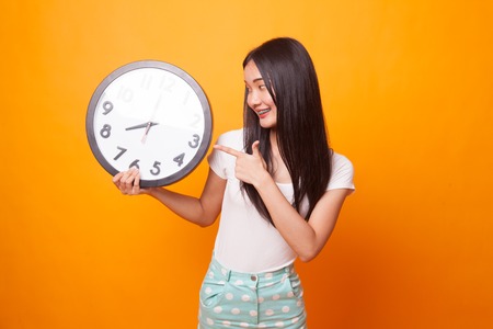 Young Asian woman point to a clock on bright yellow backgroundの写真素材