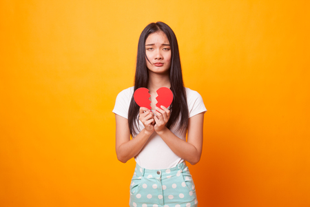 Beautiful young Asian woman with broken heart on bright yellow backgroundの写真素材