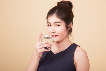Young Asian woman with a glass of drinking water  on beige backgroundの写真素材