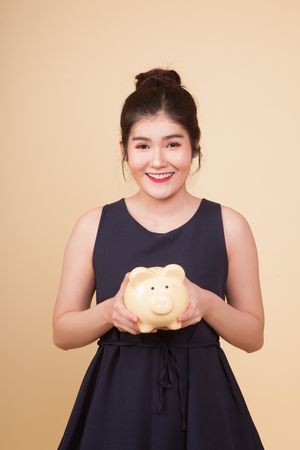Young Asian woman with a pig coin bank  on beige backgroundの写真素材