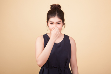Young Asian woman  holding her nose because of a bad smell  on beige backgroundの写真素材