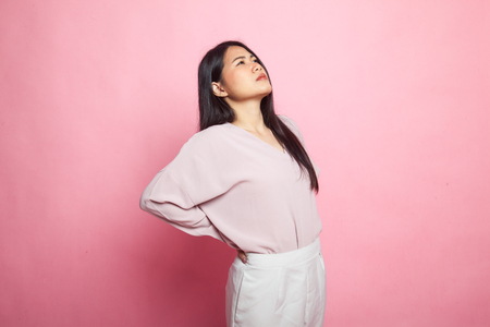 Young Asian woman got back pain on pink backgroundの写真素材